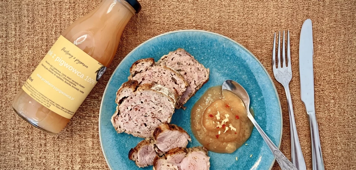 Sok z pigwowca i pieczona polędwiczka wieprzowa z sosem jabłkowym na niebieskim talerzu, sztućce obok.