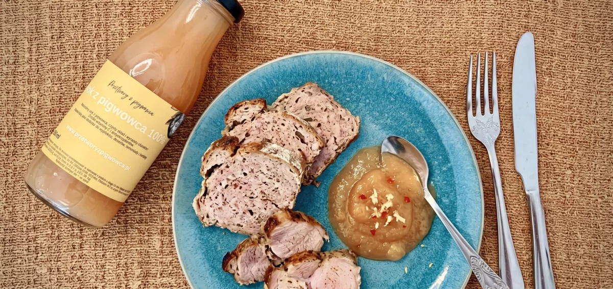 Sok z pigwowca i pieczona polędwiczka wieprzowa z sosem jabłkowym na niebieskim talerzu, sztućce obok.