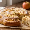 Domowe ciasto drożdżowe z jabłkami i pigwowcem, posypane kruszonką, na drewnianym stole, z jabłkami w tle.